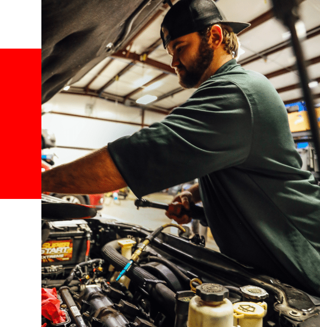 fluid maintenance services at Barrett Automotive image of technician with hat on backwards checking engine fluid on vehicle in shop