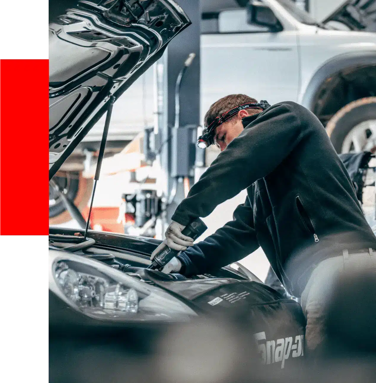 A mechanic wearing a headlamp works under the hood of a car in an auto repair shop, providing reliable car engine repair services.